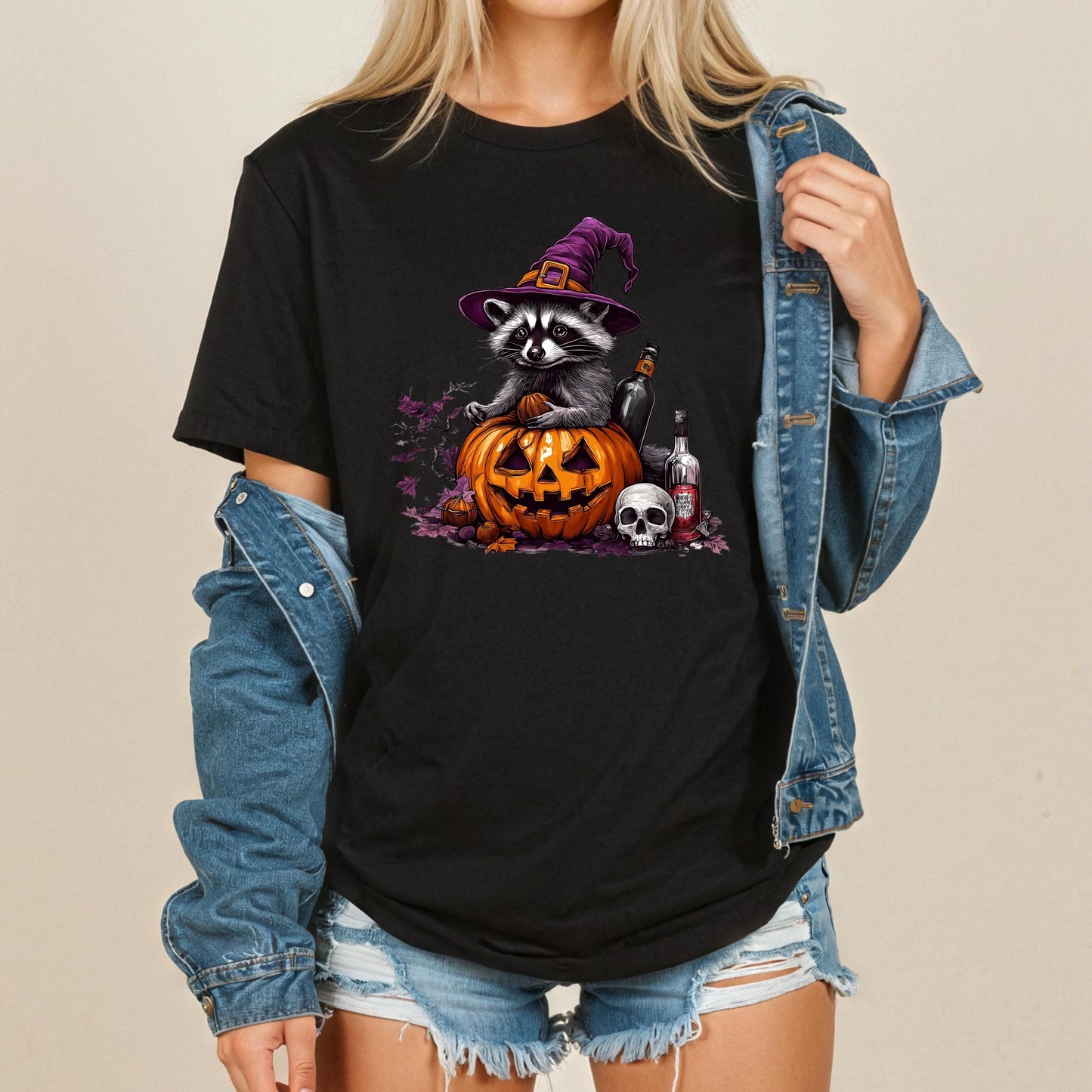 A woman wearing a black t-shirt with a Halloween-themed graphic of a raccoon wearing a witch's hat and sitting in a carved pumpkin.