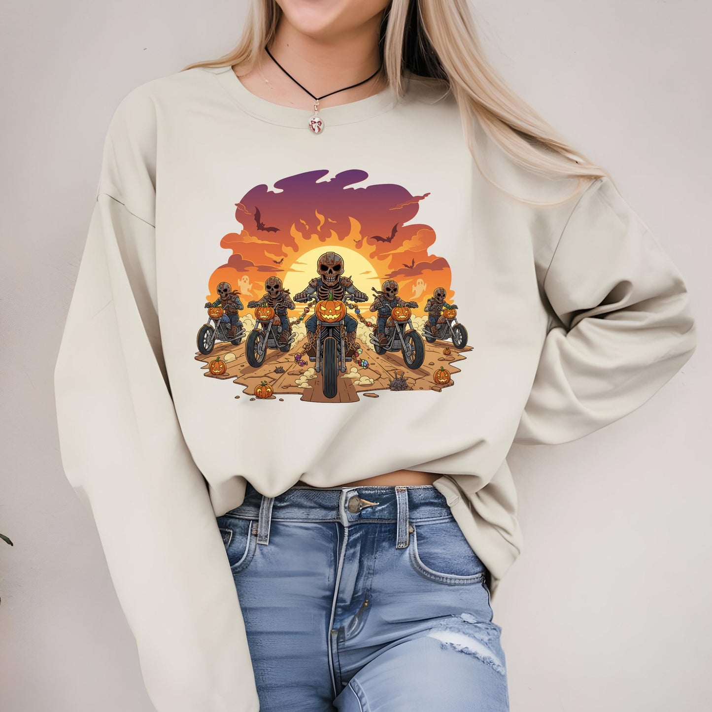 A woman wearing a white sweatshirt with a graphic design of a group of people riding motorcycles against a sunset background.