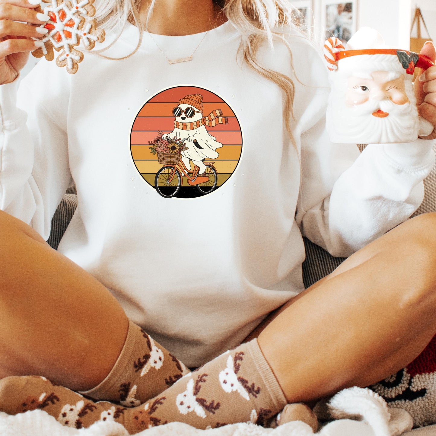 A person wearing a white sweater with a graphic of a ghost riding a bicycle, holding a mug with a Santa Claus face, and wearing patterned socks.