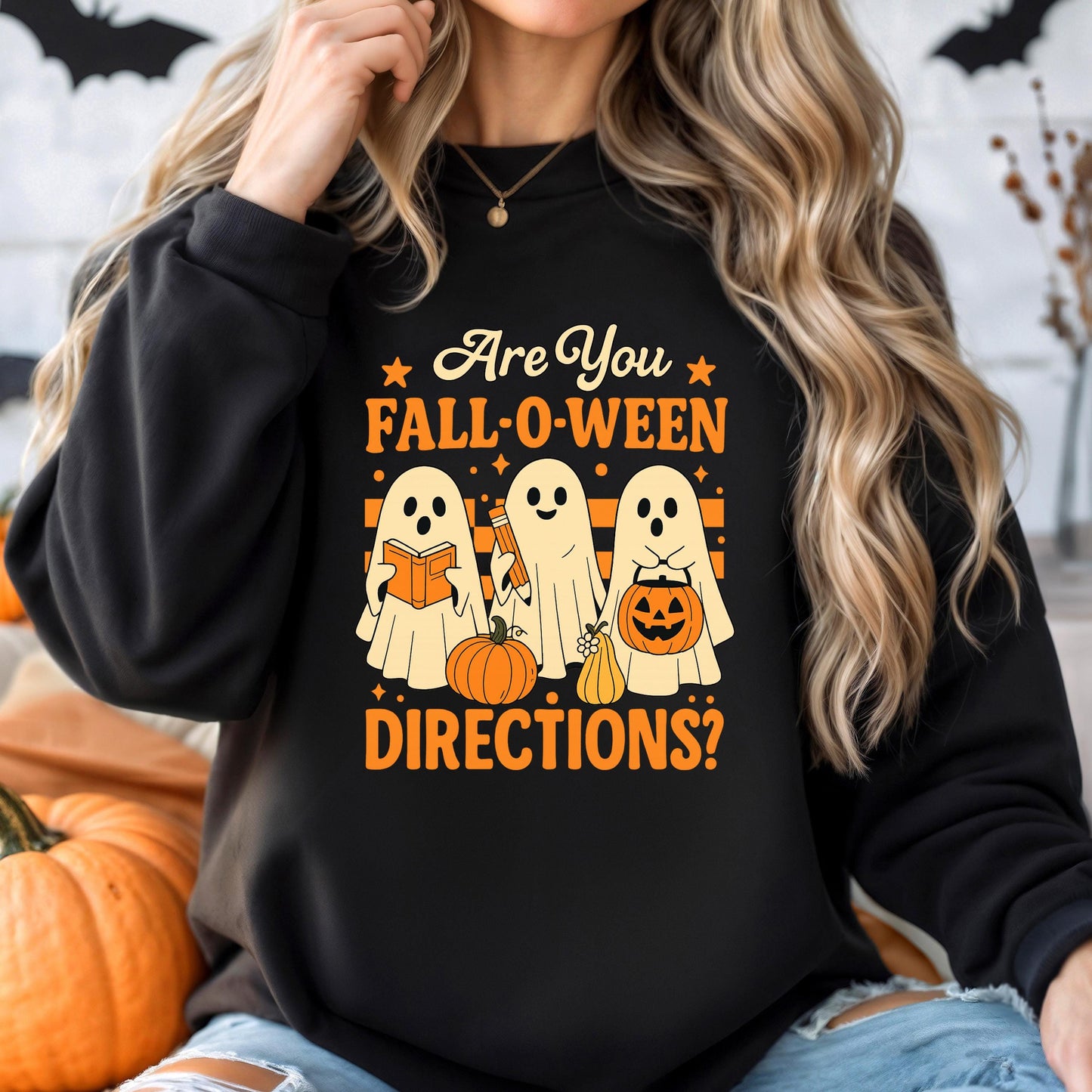 A woman wearing a black sweatshirt with a Halloween-themed graphic design featuring three ghostly figures and a pumpkin.