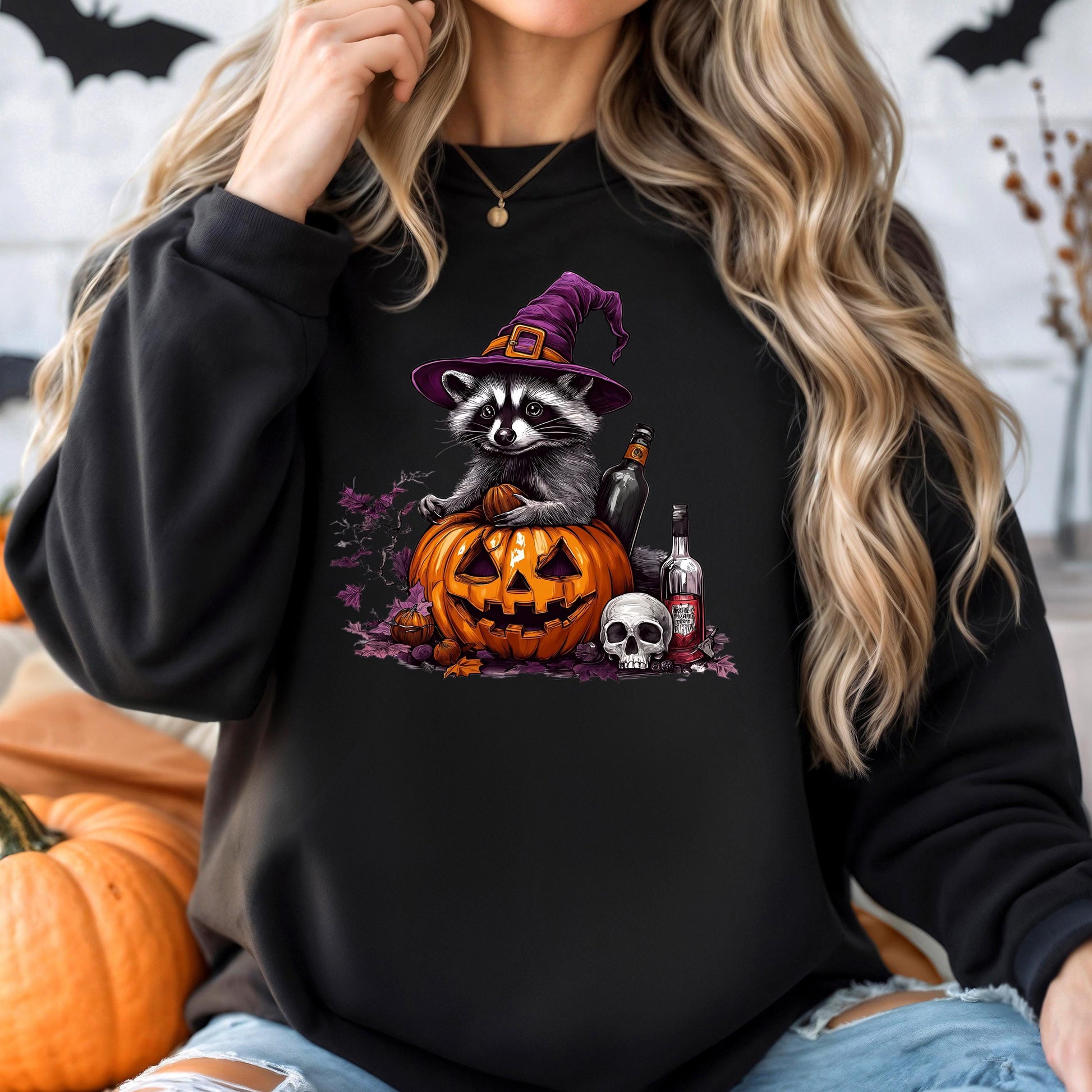 A woman wearing a black sweatshirt with a Halloween-themed graphic of a raccoon wearing a witch's hat and sitting on a carved pumpkin.