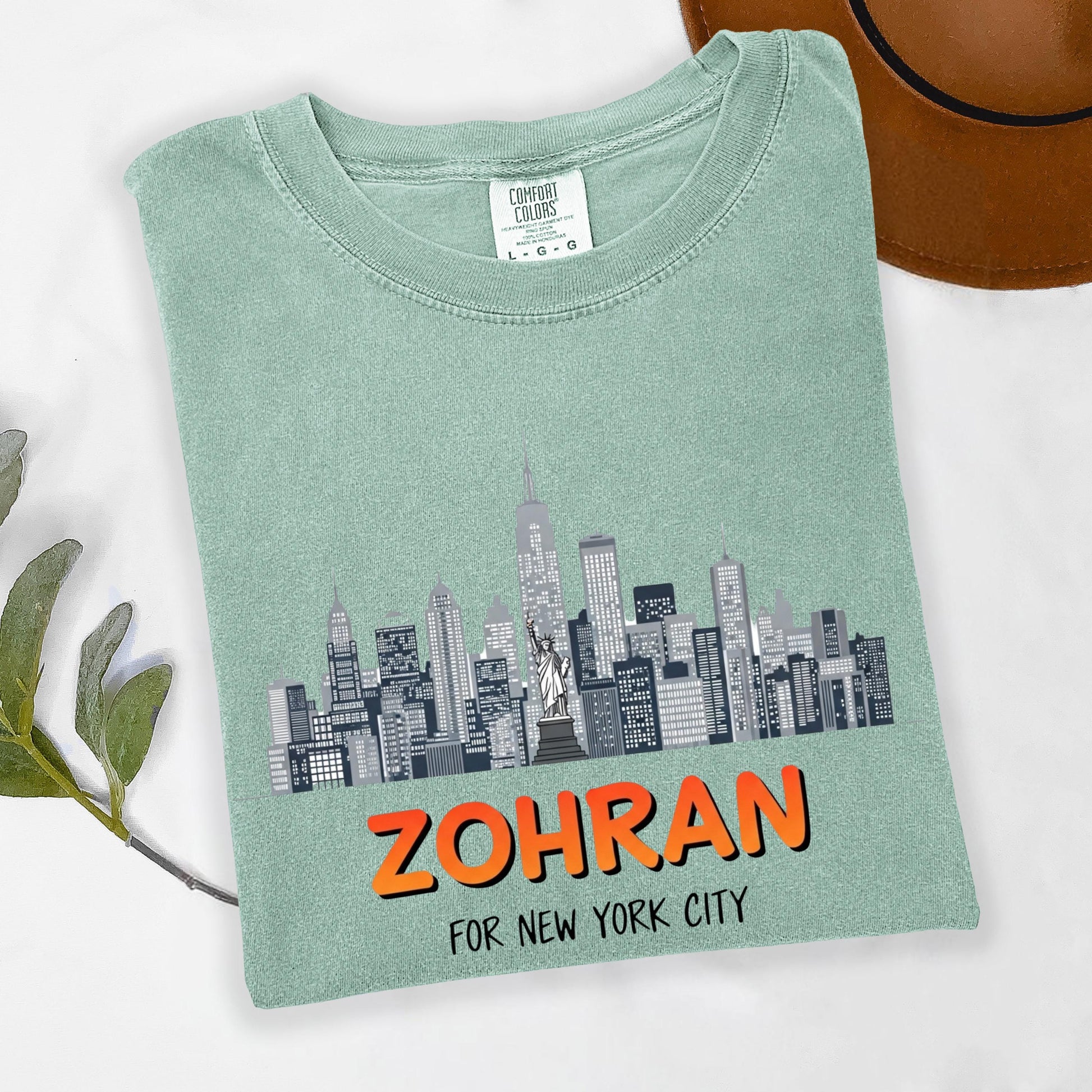 A green t-shirt with a graphic of a city skyline and the text "ZOHRAN FOR NEW YORK CITY" printed on it.