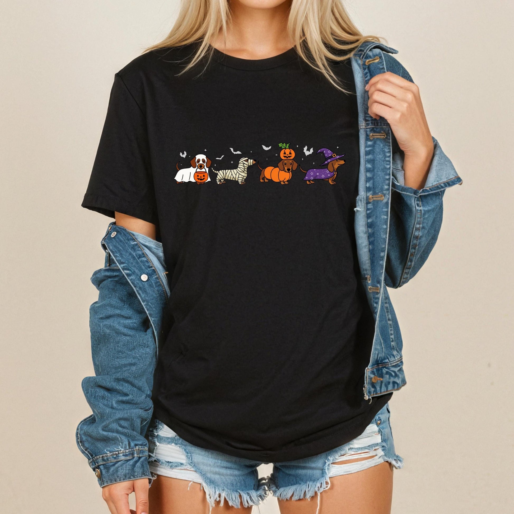 A woman wearing a black t-shirt with a graphic of a line of cartoon dogs and a pumpkin, along with a denim jacket.