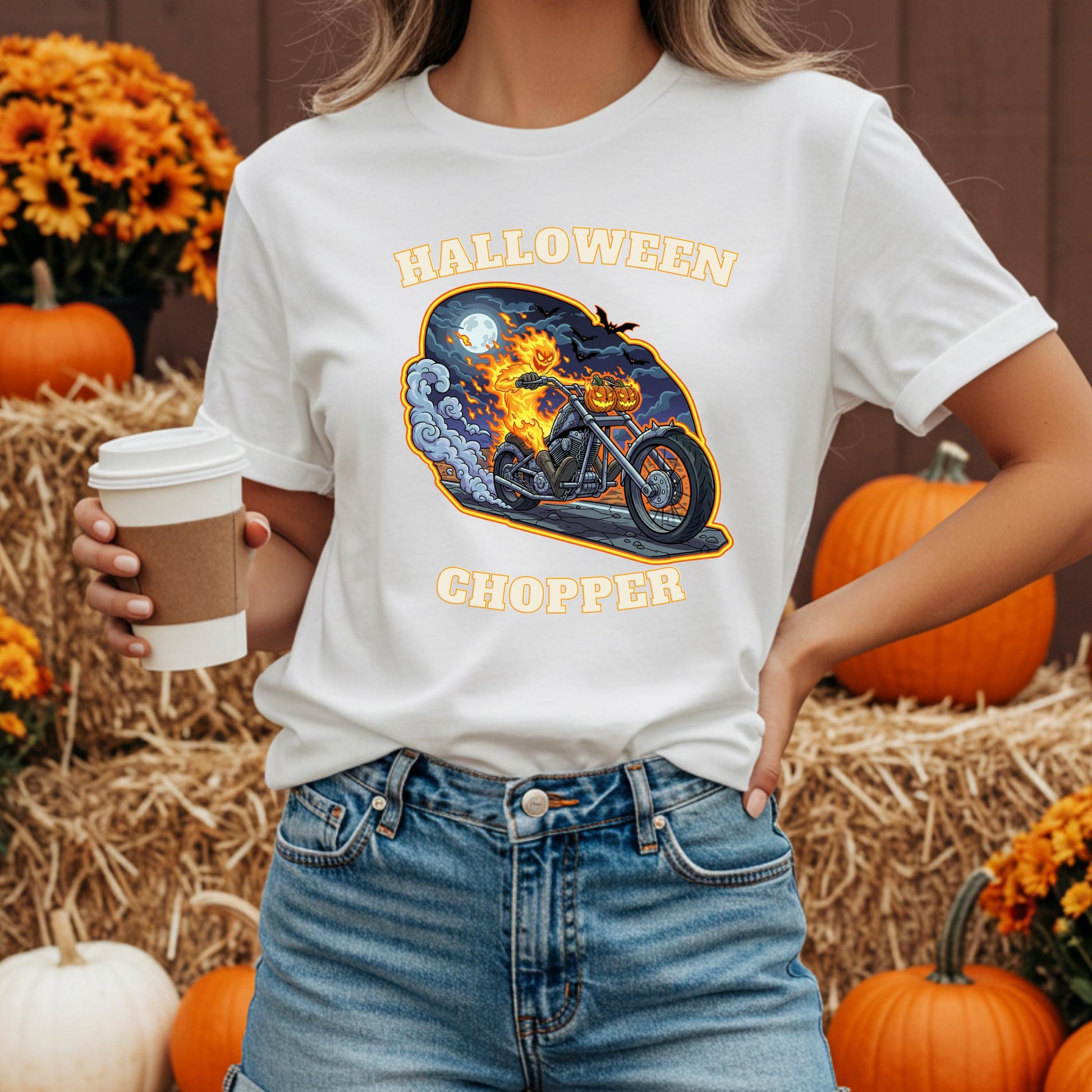 A woman wearing a white t-shirt with a graphic of a motorcycle and the text "Halloween Chopper" is holding a coffee cup in front of a hay bale and pumpkins.