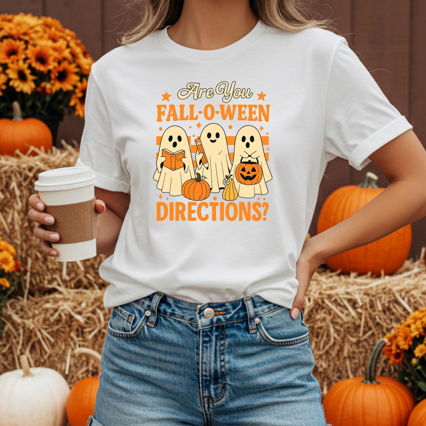 A woman wearing a white t-shirt with a graphic design of three ghostly figures and Halloween-themed objects, holding a coffee cup.