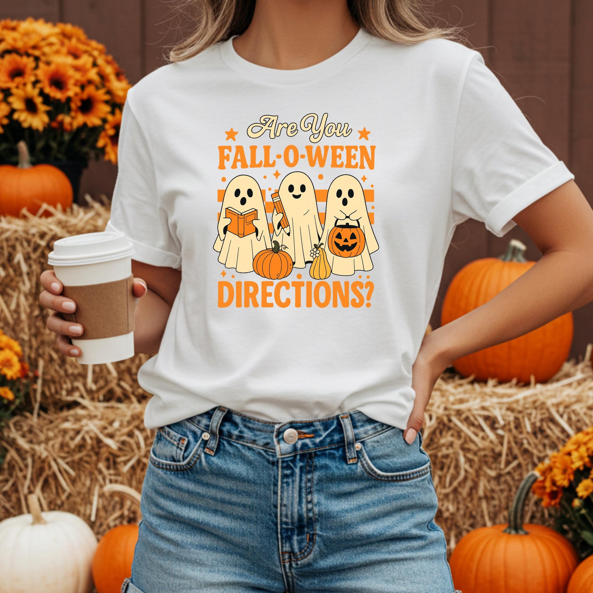 A woman wearing a white t-shirt with a graphic design of three ghostly figures and Halloween-themed objects, holding a coffee cup.