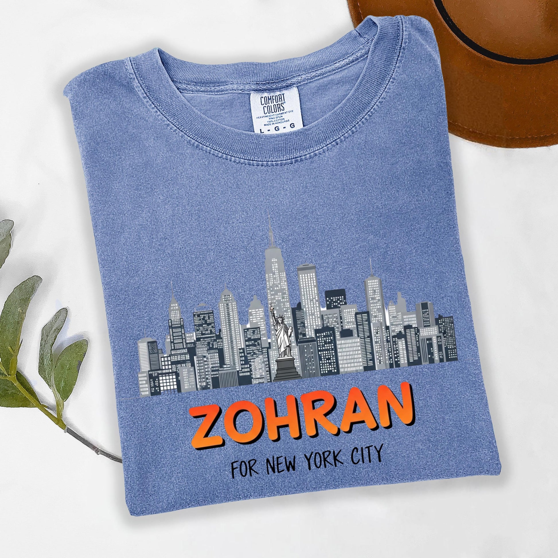 A blue t-shirt with a graphic of a city skyline and the text "ZOHRAN FOR NEW YORK CITY" printed on it.