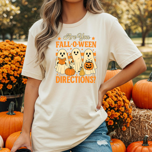 A woman wearing a white t-shirt with a graphic design of three ghostly figures holding pumpkins and a pumpkin, standing in front of a background of orange pumpkins and flowers.