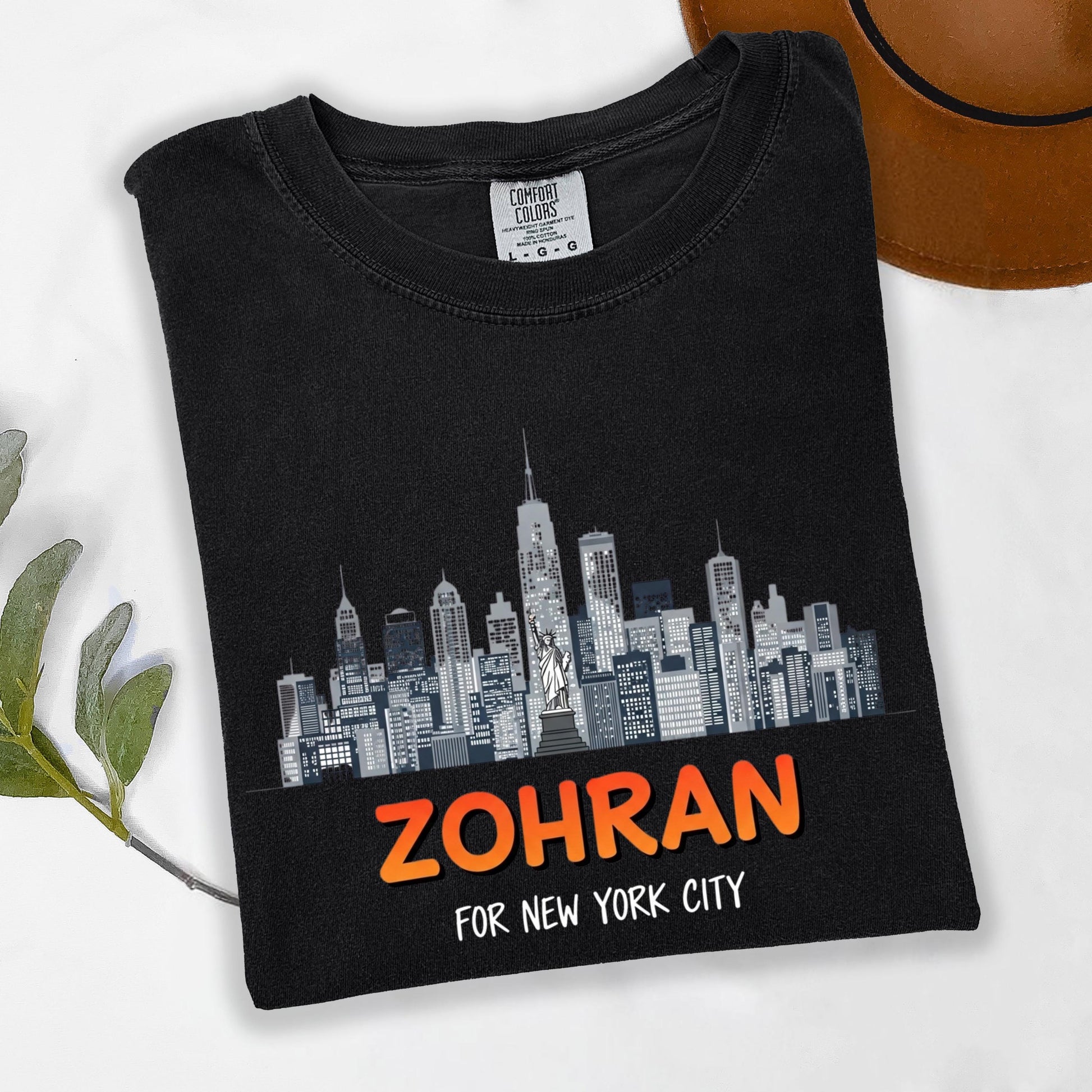 A black t-shirt with a graphic design of a city skyline printed on it, along with the text "Zohran for New York City" printed below.