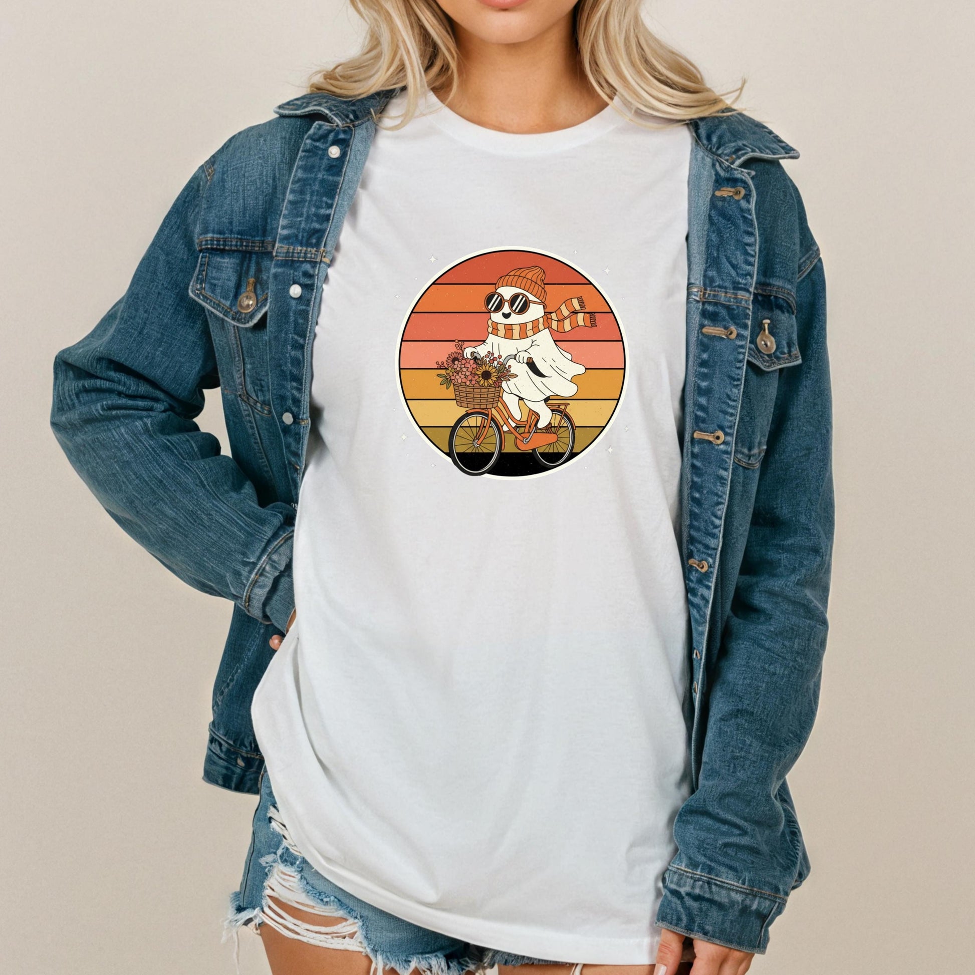 A woman wearing a denim jacket and a white t-shirt with a graphic of a ghost riding a bicycle.