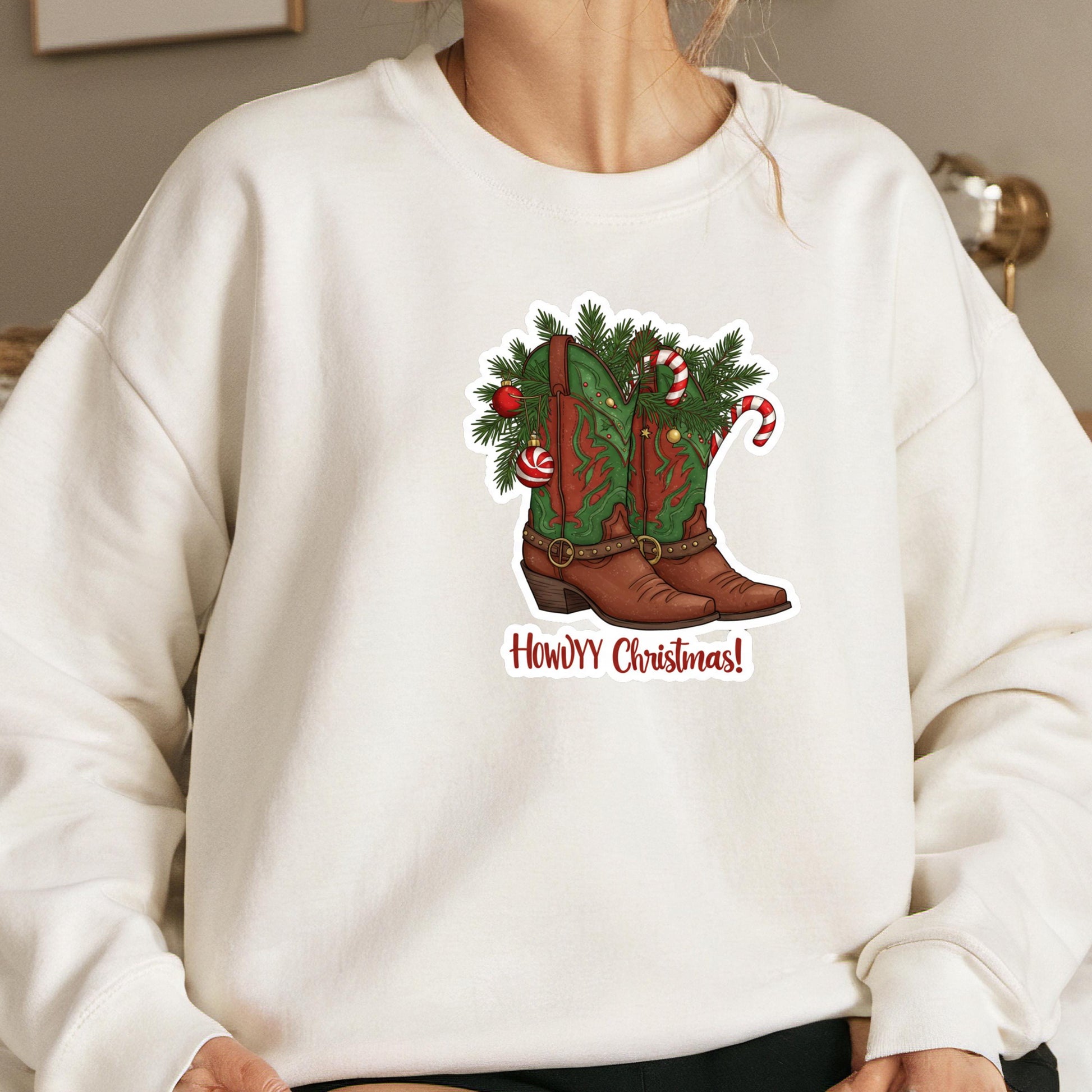 A white sweatshirt with a graphic of a pair of red cowboy boots adorned with Christmas decorations, including candy canes and pine branches.