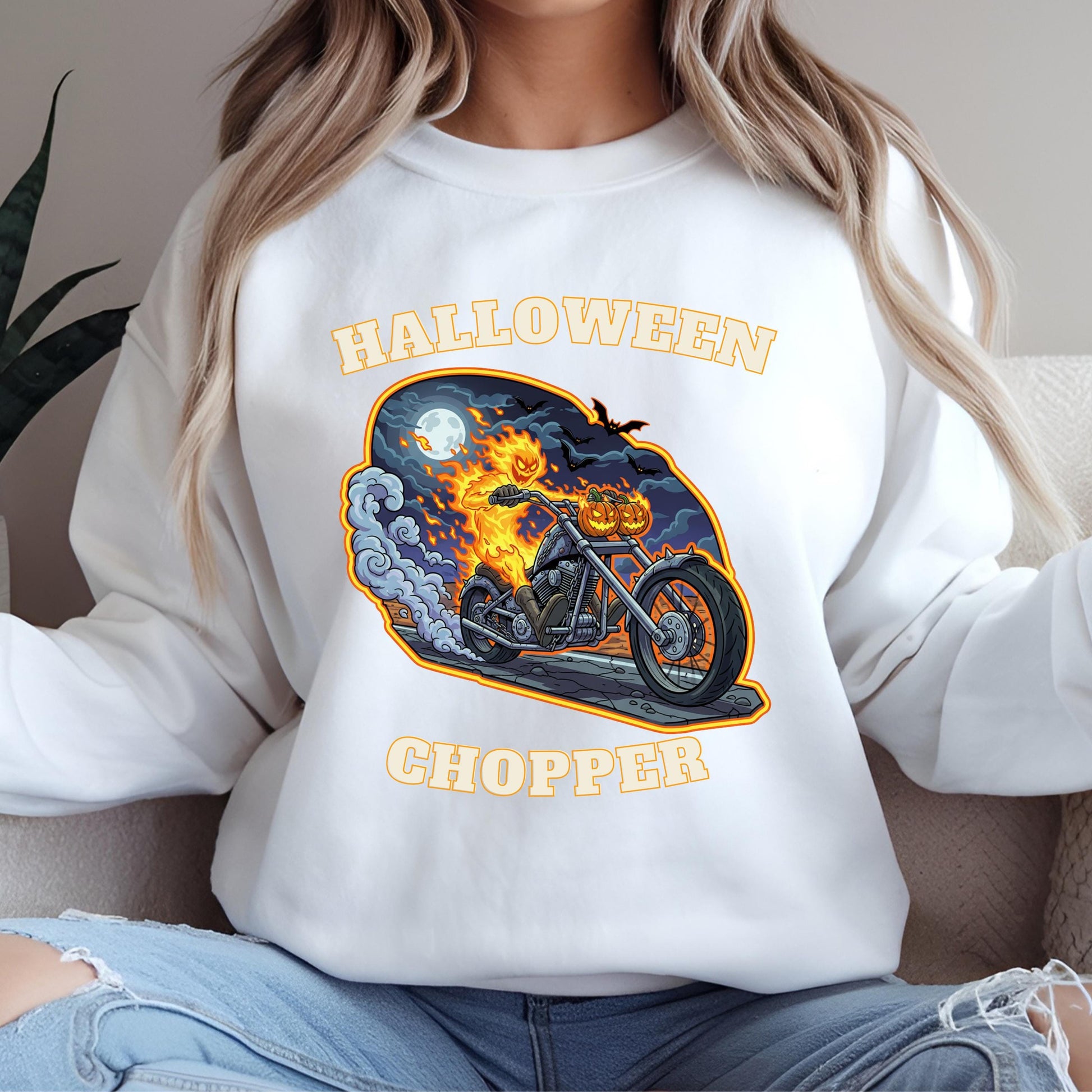 A white sweatshirt with a Halloween-themed graphic design depicting a motorcycle with a jack-o-lantern on the handlebars.