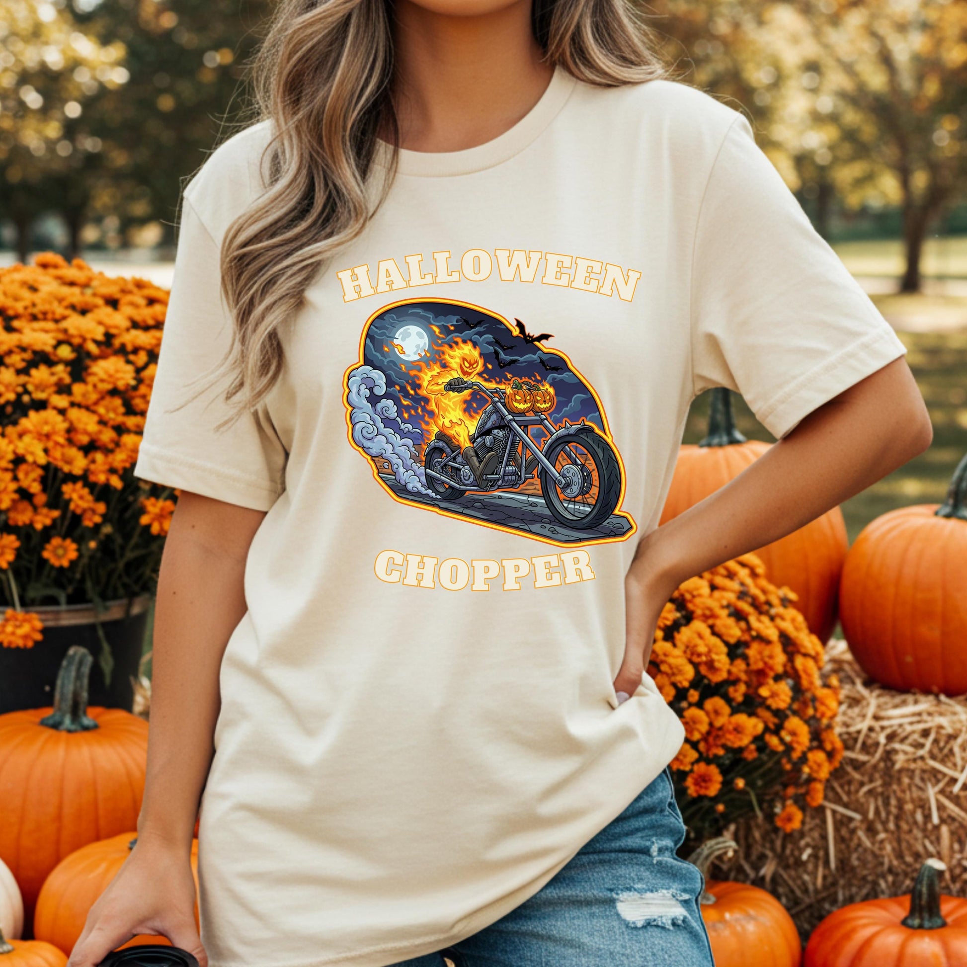 A woman wearing a white t-shirt with a graphic of a motorcycle and the text "Halloween Chopper" is standing in front of a display of pumpkins and flowers.