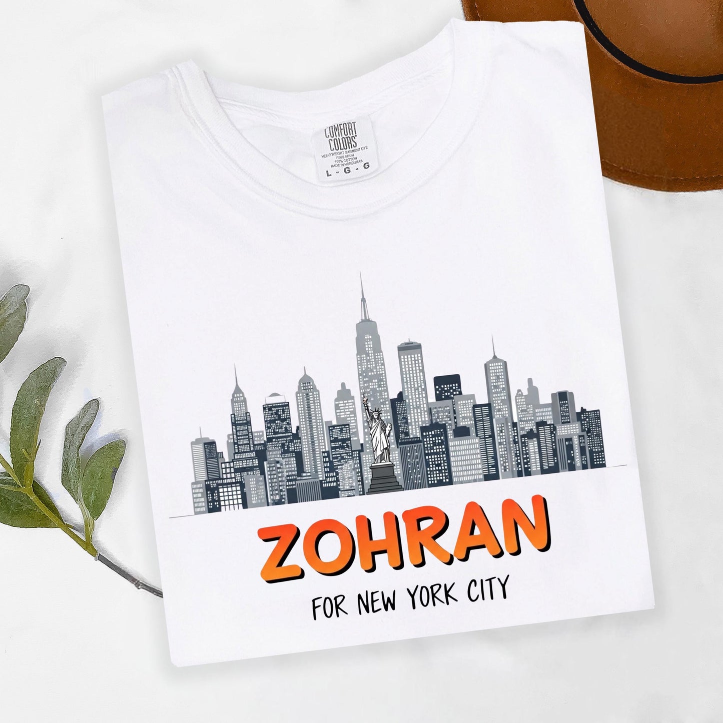 A white t-shirt with a graphic design depicting the New York City skyline, along with the text "ZOHRAN FOR NEW YORK CITY" printed on it.