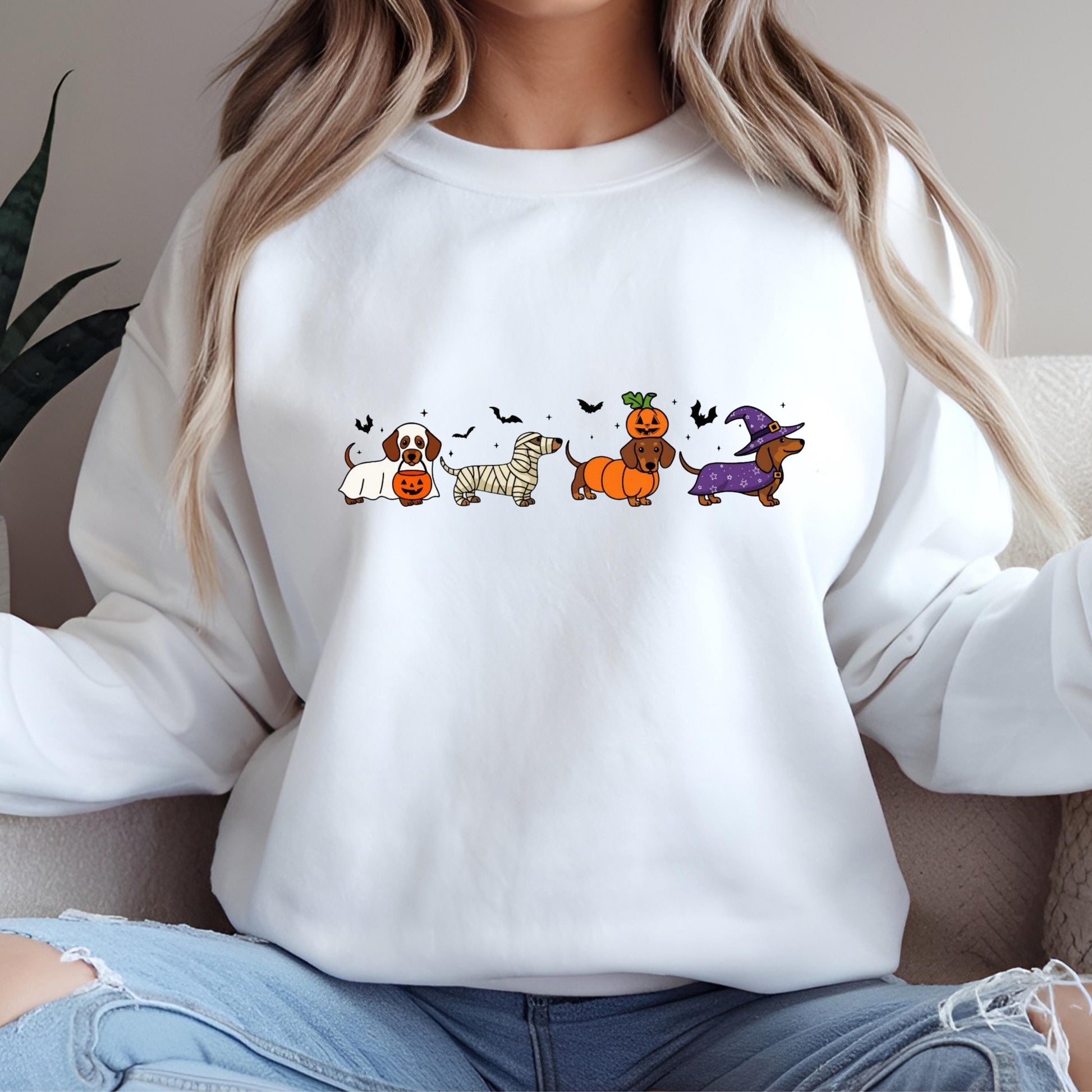 A woman wearing a white sweatshirt with a graphic design of cartoon dogs in Halloween costumes.