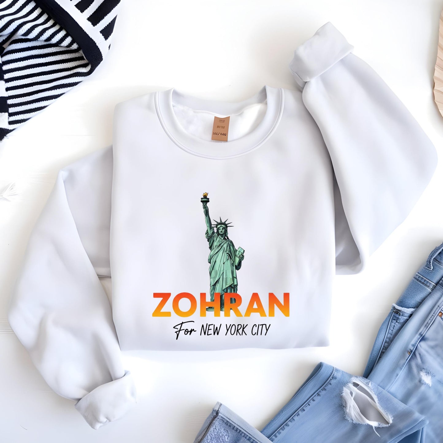 A white sweatshirt with a graphic of the Statue of Liberty and the text "ZOHRAN For New York City" printed on it, along with a small tag.