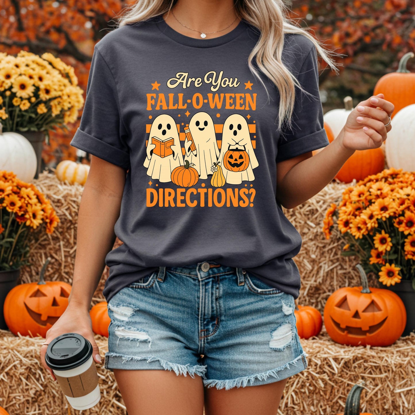 A woman wearing a t-shirt with a Halloween-themed graphic and text, standing in front of a hay bale and pumpkins.