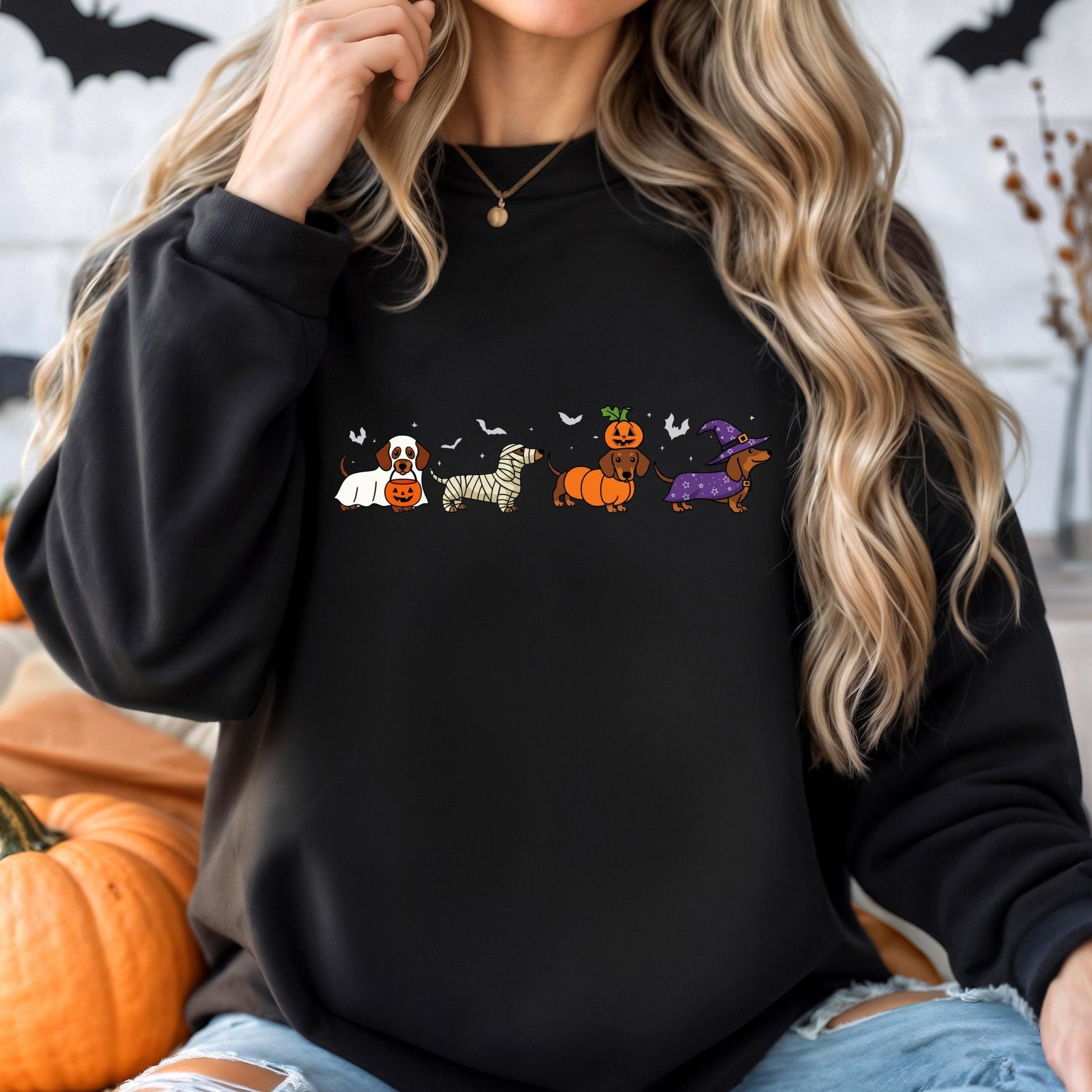 A woman wearing a black sweatshirt with a graphic design of four cartoon dogs dressed in Halloween costumes.