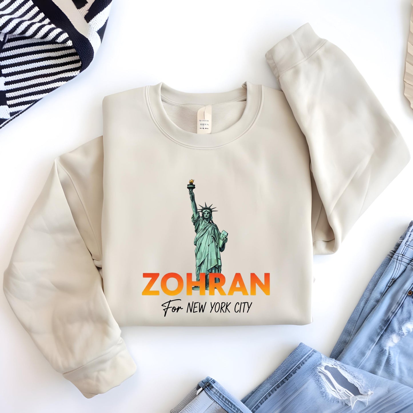 A beige sweater with a graphic of the Statue of Liberty and the text "ZOHRAN For New York City" printed on it, along with a small tag.