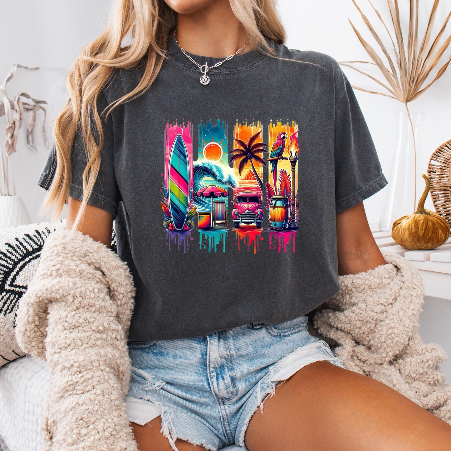 A person wearing a gray t-shirt with a colorful graphic design featuring a surfboard, palm tree, and other tropical elements.