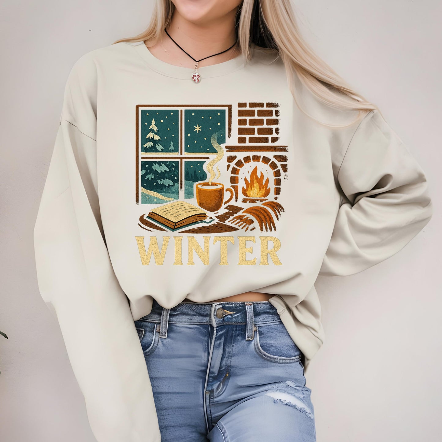 A woman wearing a white sweater with a graphic design depicting a cozy winter scene, including a fireplace, a cup of coffee, and a book.