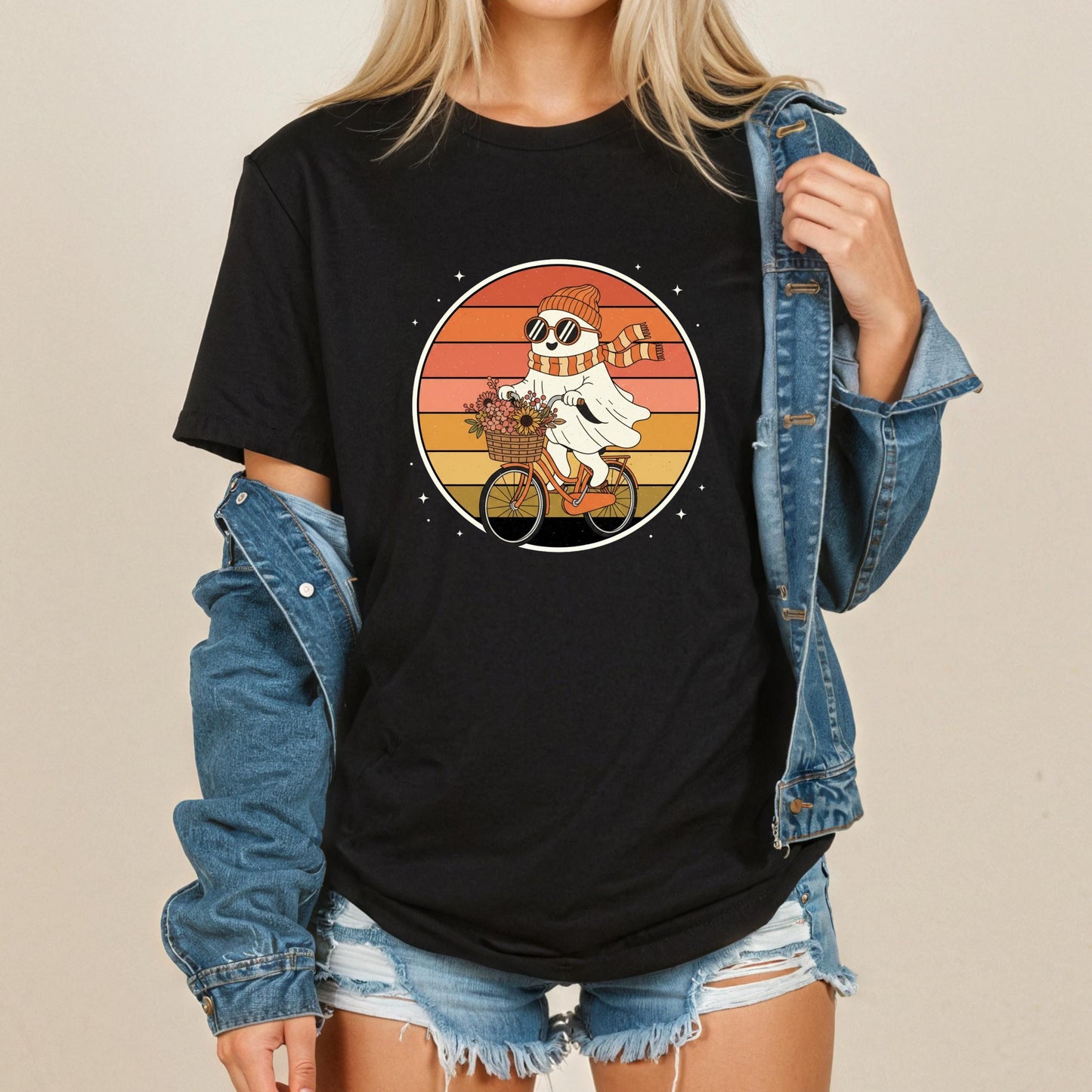 A woman wearing a black t-shirt with a graphic of a person riding a bicycle and a scarf, along with denim shorts and a denim jacket.