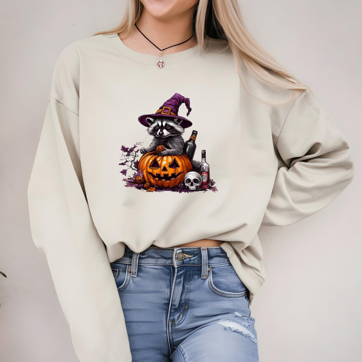 A woman wearing a white sweater with a graphic of a raccoon wearing a witch&#39;s hat and holding a carved pumpkin, along with a skull and crossbones.