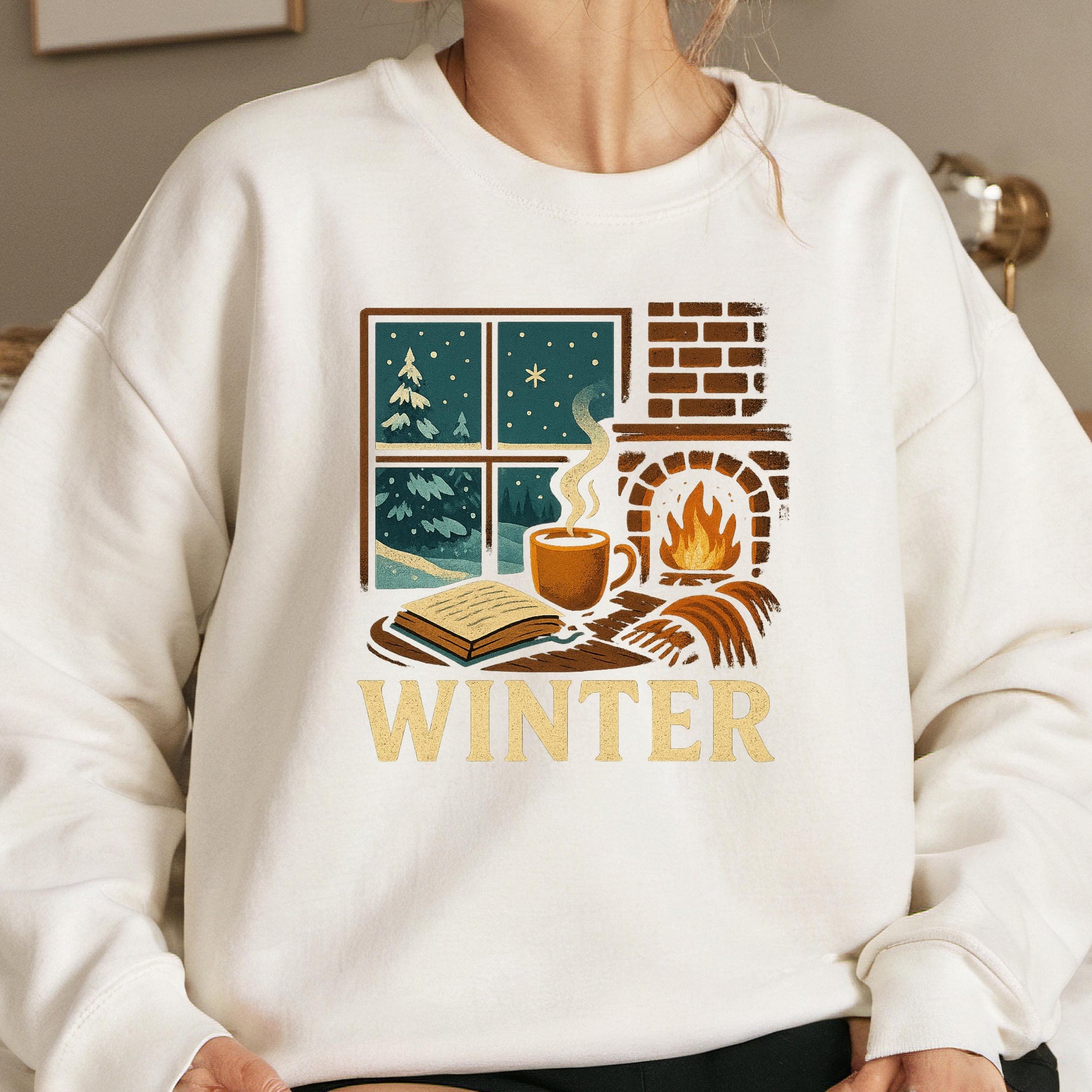 A white sweatshirt with a graphic design depicting a cozy winter scene, including a fireplace, a cup of coffee, and a book.