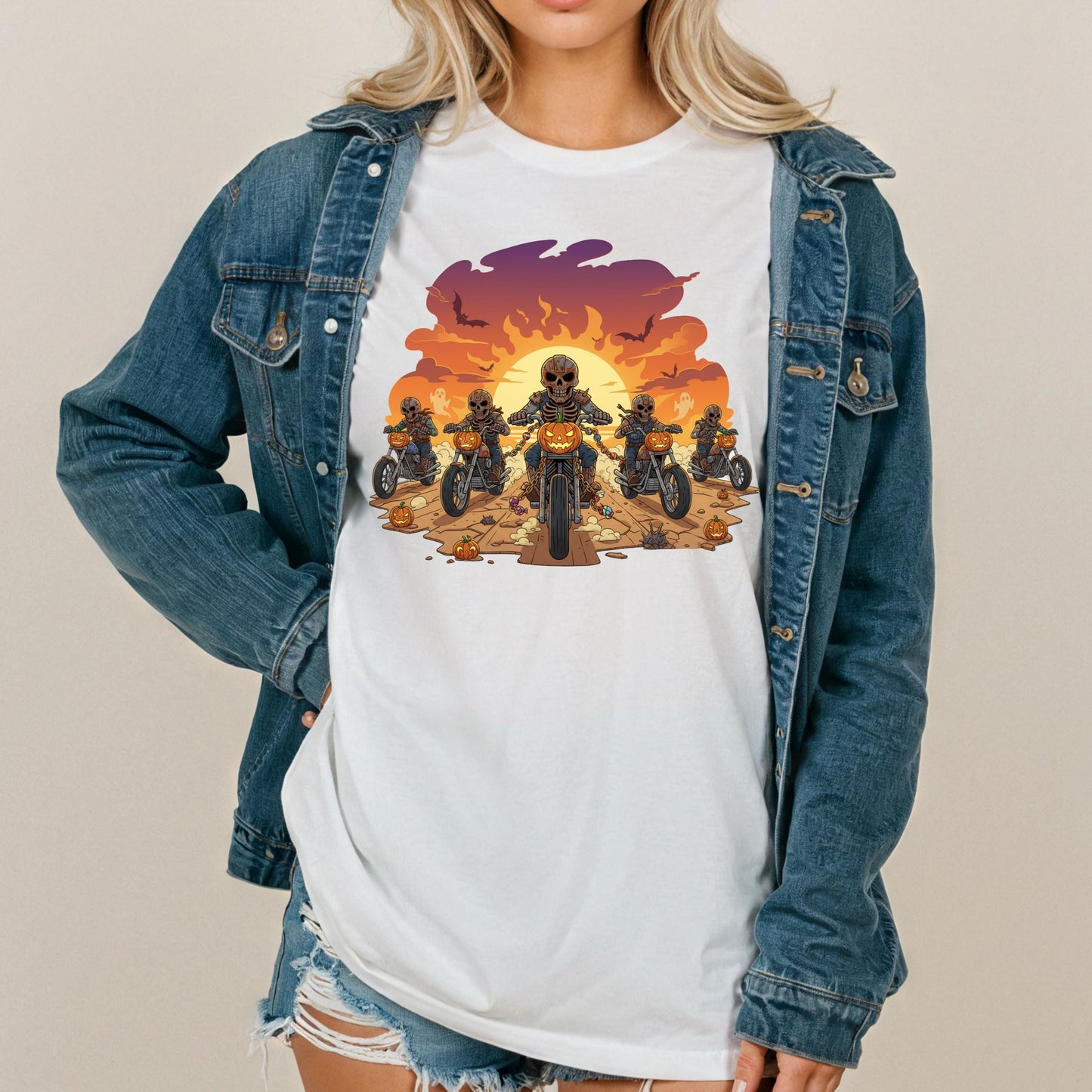 A woman wearing a denim jacket and a white t-shirt with a graphic design of a group of people riding motorcycles against a sunset background.