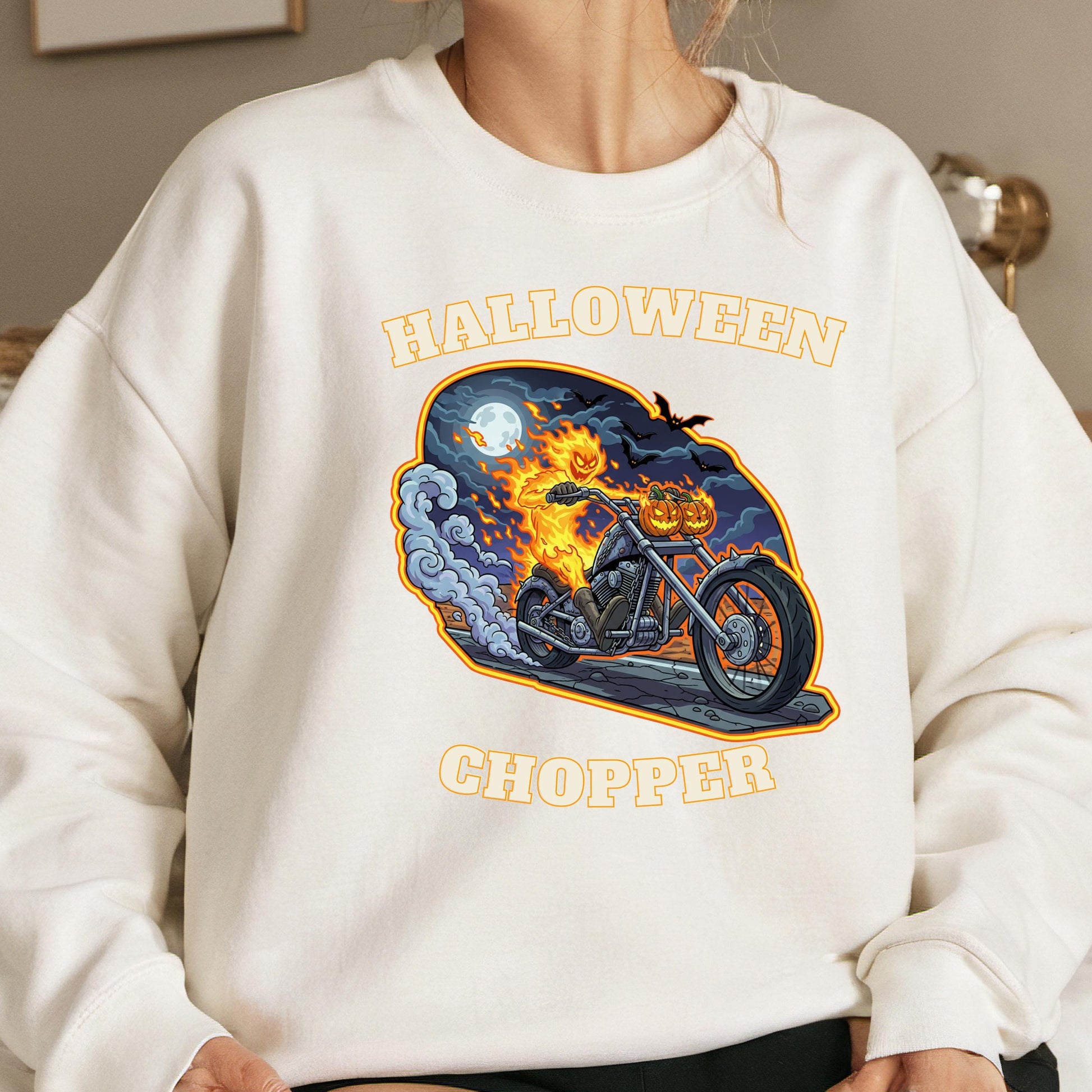 A white sweatshirt with a Halloween-themed graphic design depicting a motorcycle with a jack-o-lantern rider, along with the text &quot;HALLOWEEN CHOPPER&quot; printed on it.