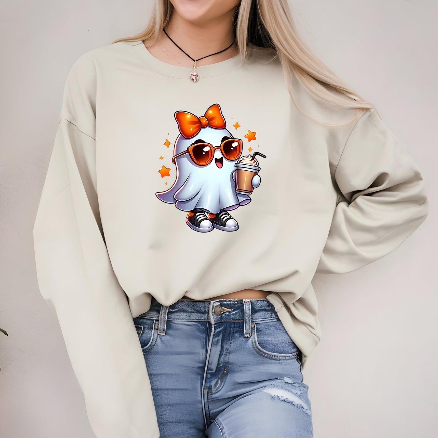 A woman wearing a white sweater with a cartoon ghost graphic and sunglasses, along with blue jeans.
