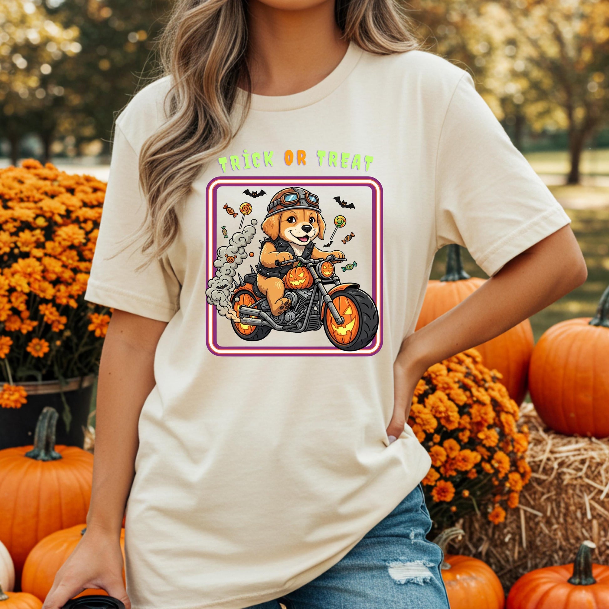 A woman wearing a white t-shirt with a graphic of a dog riding a motorcycle, surrounded by pumpkins and flowers, with the text &quot;Trick or Treat&quot; displayed.