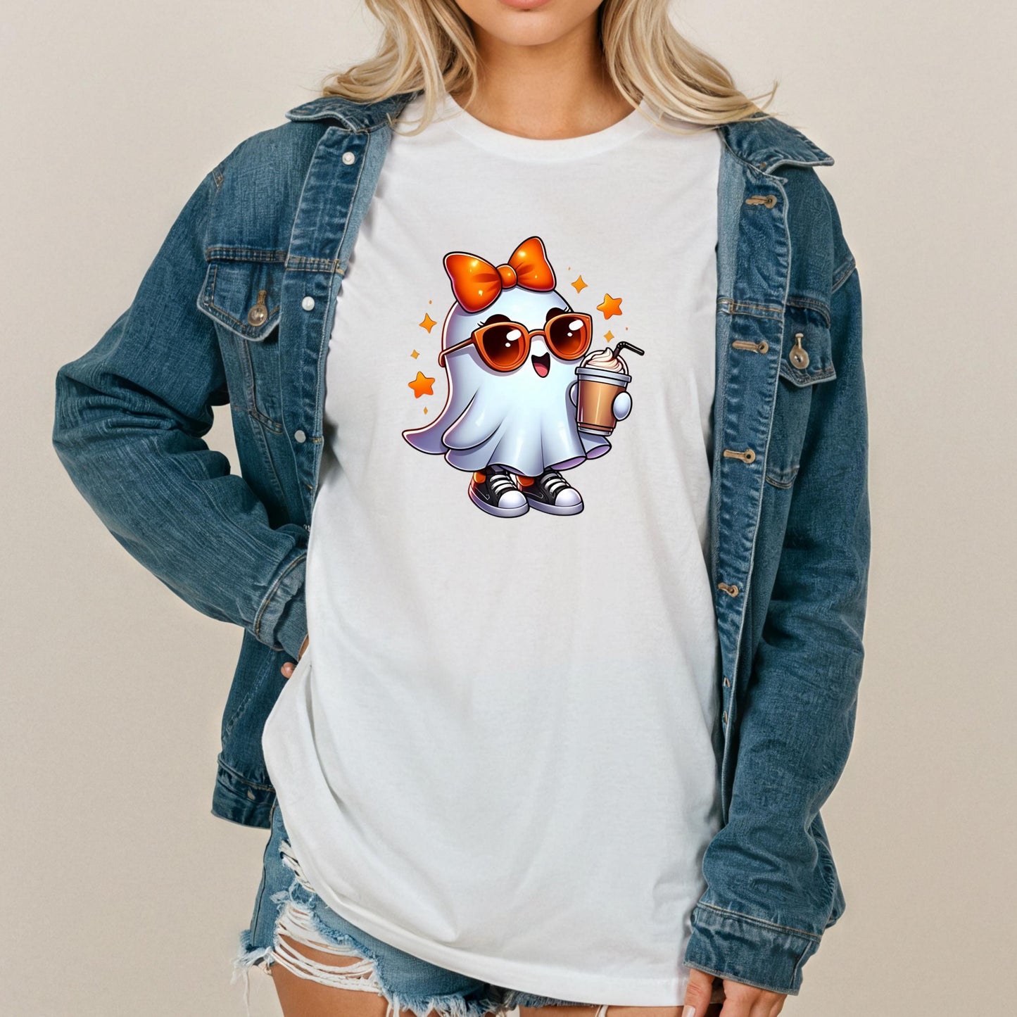 A woman wearing a denim jacket and a white t-shirt with a cartoon ghost character holding a drink and wearing sunglasses.