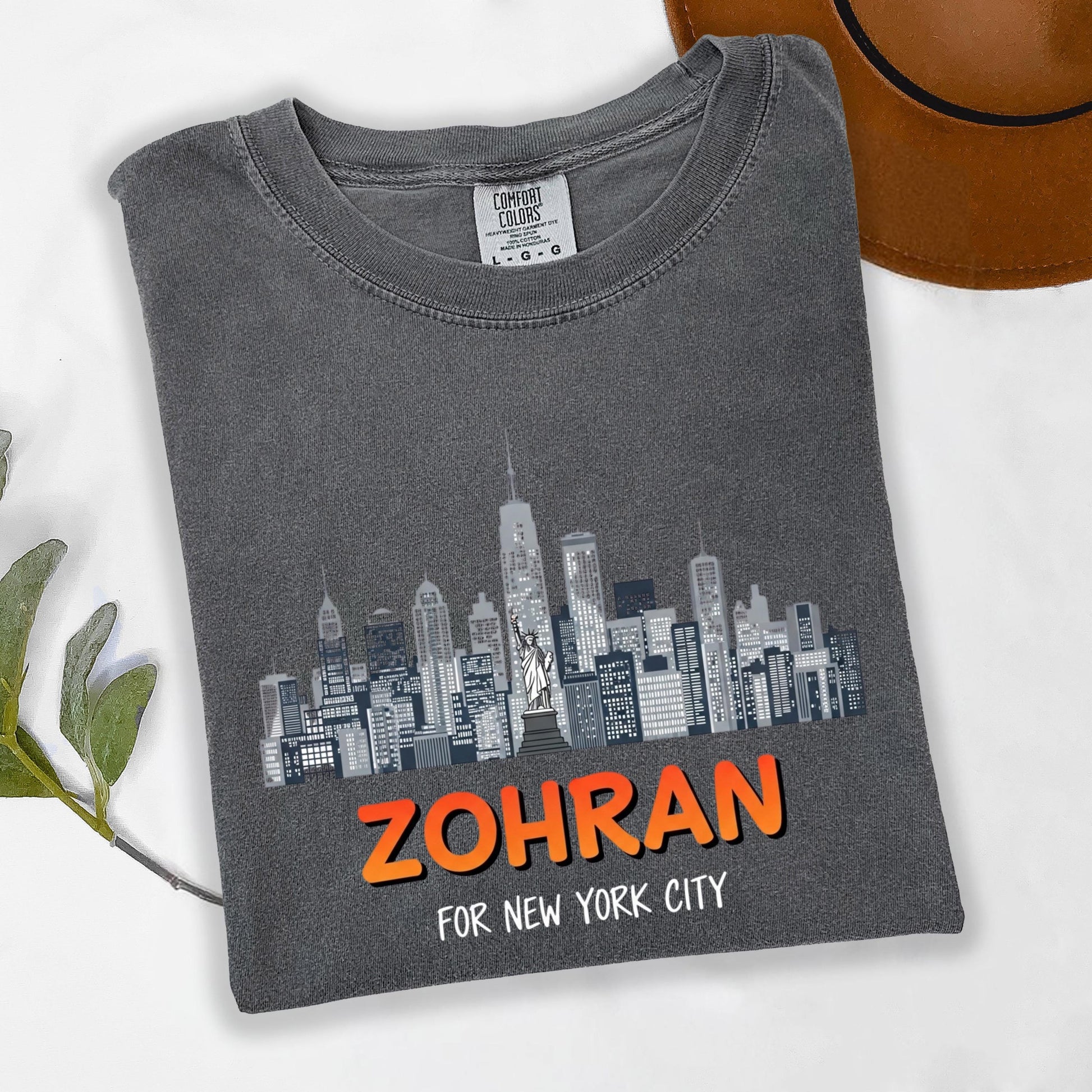 A gray t-shirt with a graphic of a city skyline printed on it, along with the text "Zohran for New York City".