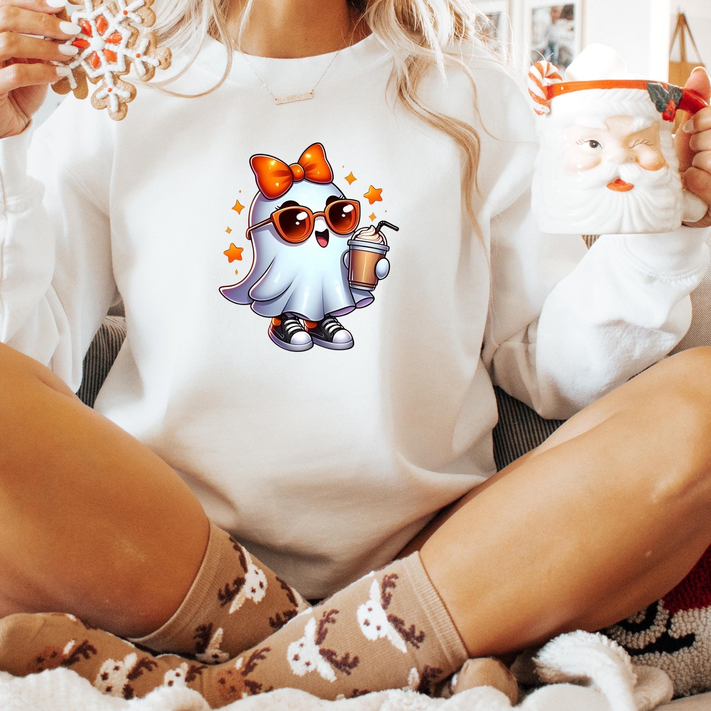 A person wearing a white sweater with a cartoon ghost character and holding a mug is sitting on a couch.