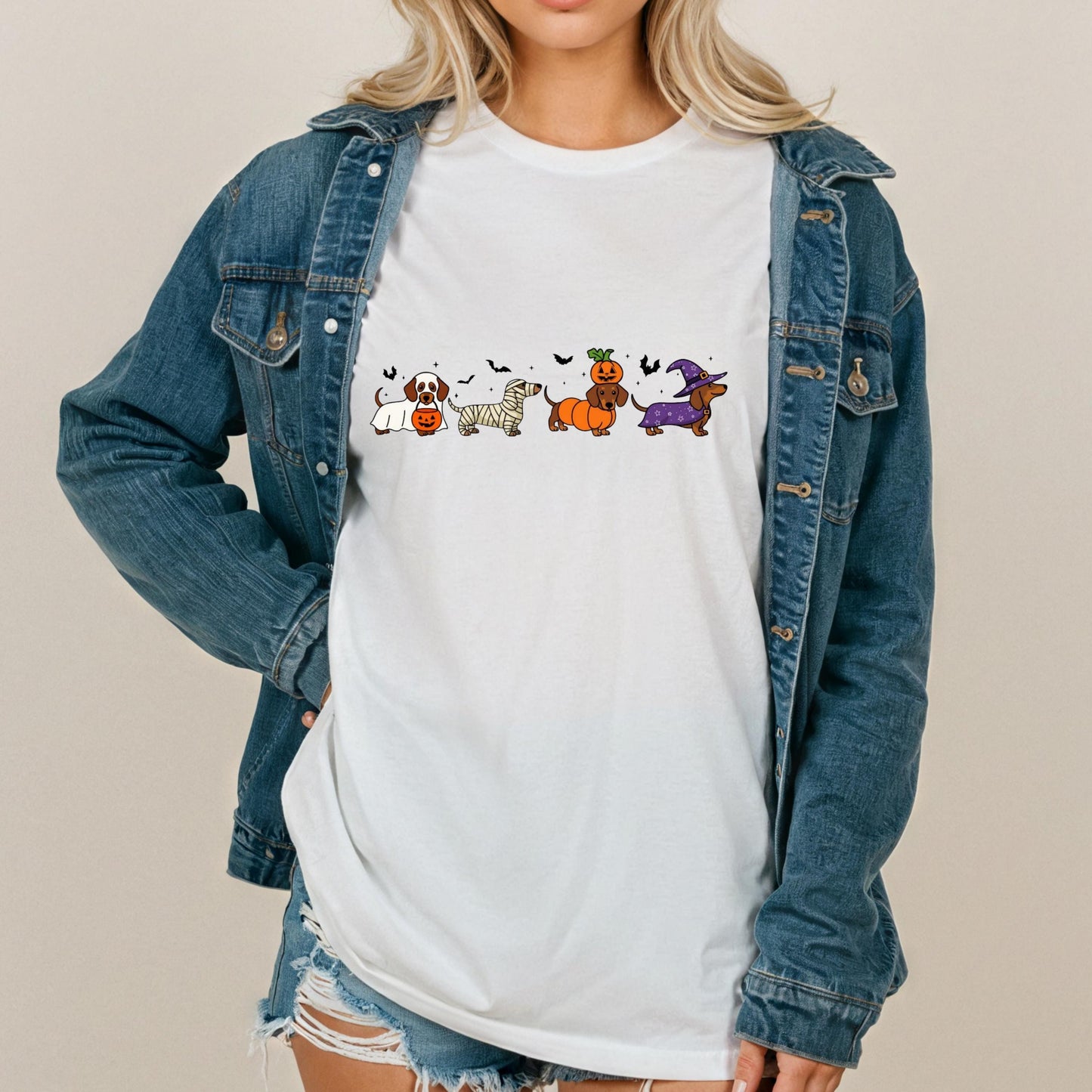 A woman wearing a denim jacket and a white t-shirt with a graphic of cartoon dogs and Halloween-themed elements.
