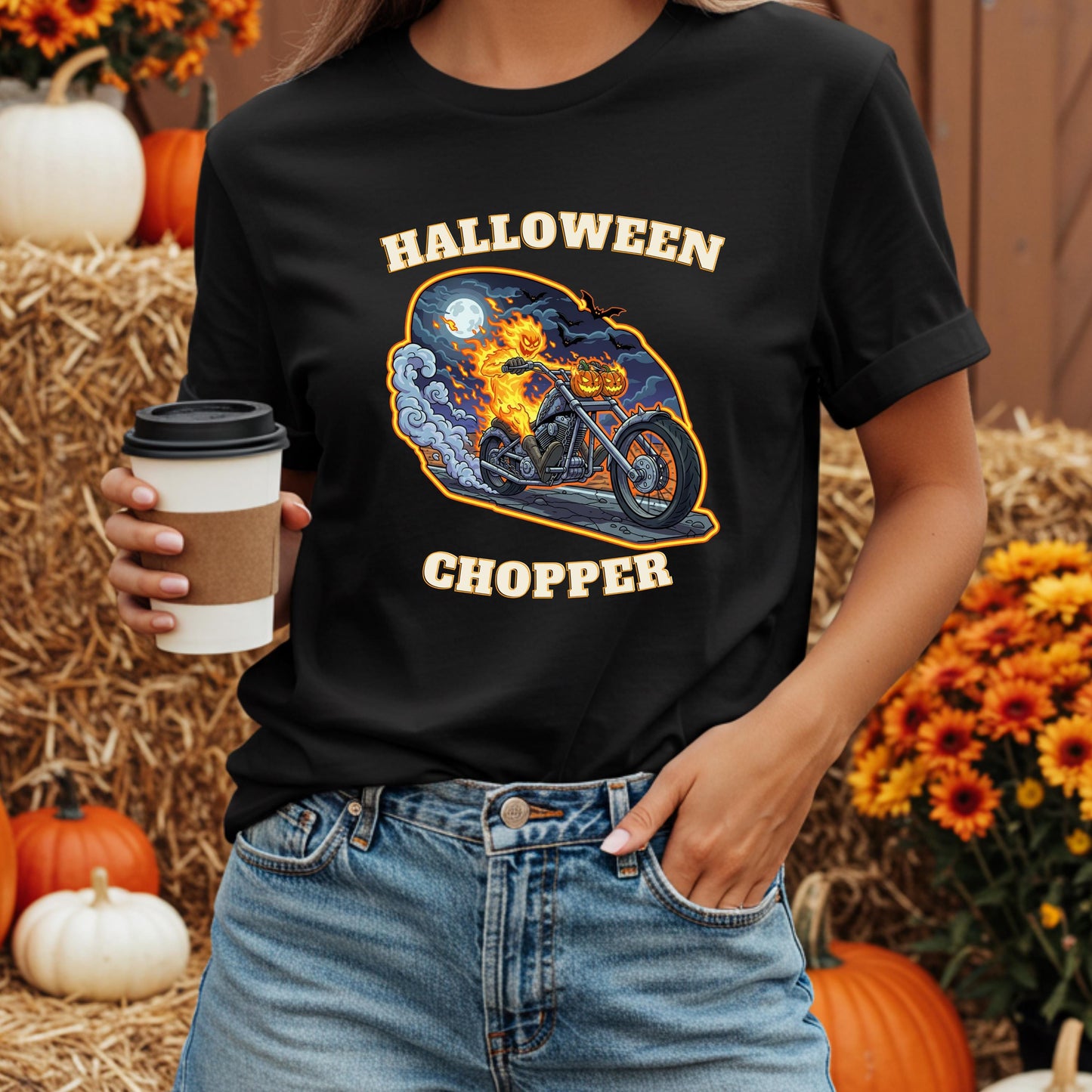 A person wearing a black t-shirt with a Halloween-themed graphic of a motorcycle and a bat, holding a coffee cup.