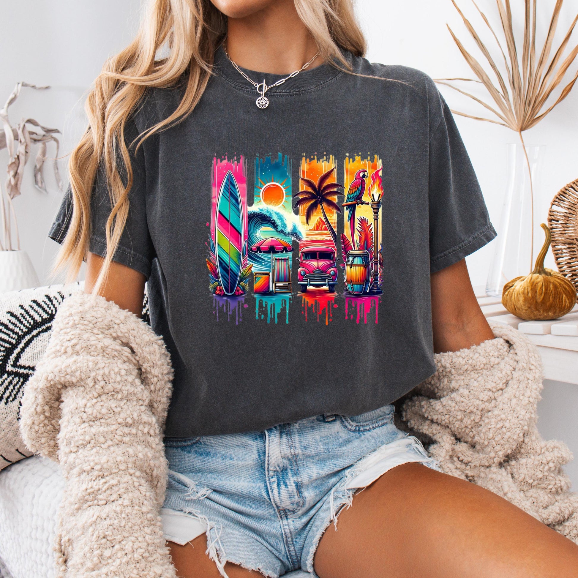 A person wearing a gray t-shirt with a colorful graphic design featuring a surfboard, palm tree, and other tropical elements.